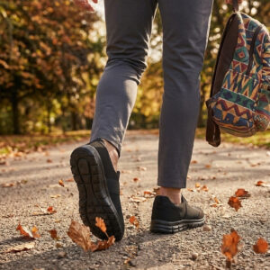 Sokakta yürüyen bir modelin ayağında siyah renkli, bağcıksız, hafif tekstil malzemeden üretilmiş erkek slip-on sneaker ayakkabı.