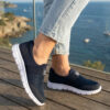 Sokakta yürüyen bir modelin ayağında siyah renkli, bağcıksız, hafif tekstil malzemeden üretilmiş erkek slip-on sneaker ayakkabı.