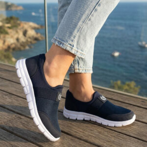 Sokakta yürüyen bir modelin ayağında siyah renkli, bağcıksız, hafif tekstil malzemeden üretilmiş erkek slip-on sneaker ayakkabı.