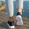 Sokakta yürüyen bir modelin ayağında siyah renkli, bağcıksız, hafif tekstil malzemeden üretilmiş erkek slip-on sneaker ayakkabı.